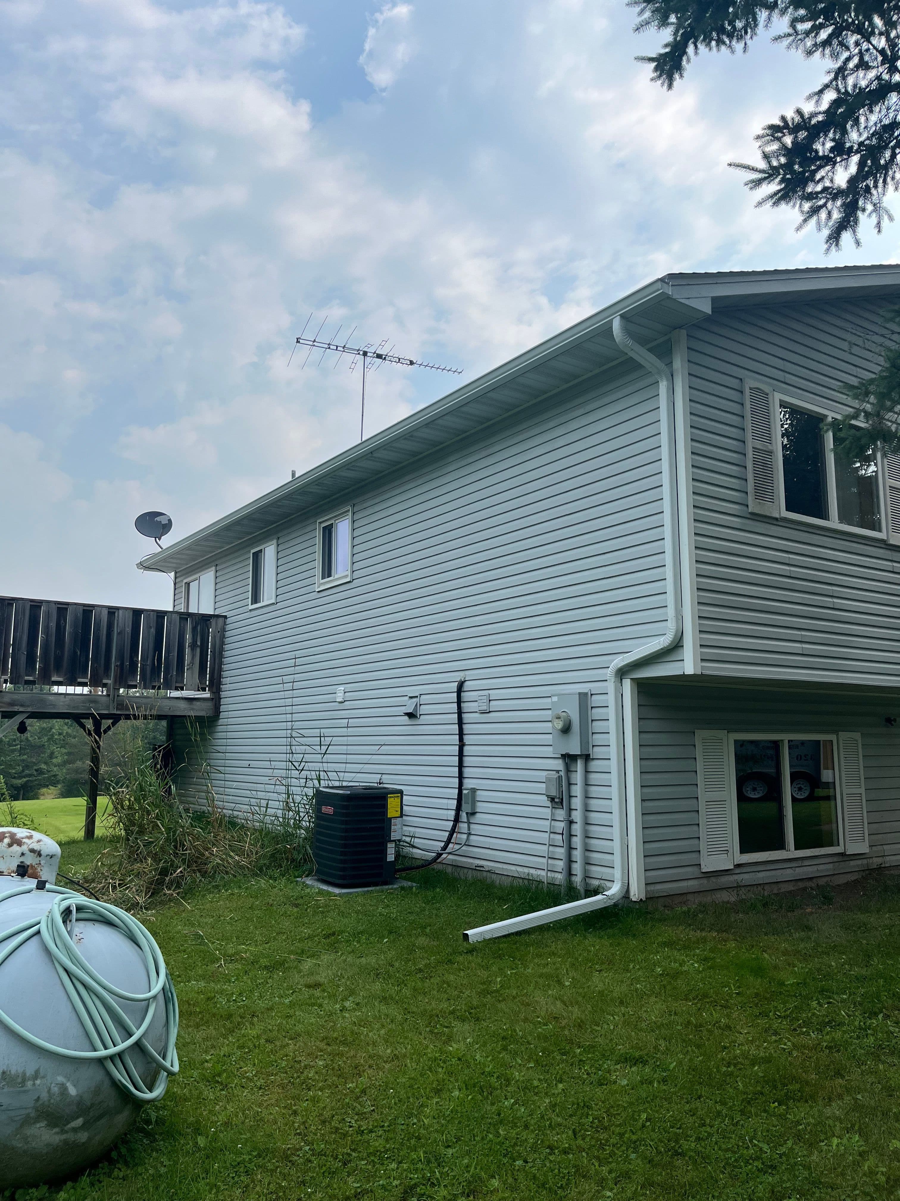 Side view of a gray house featuring a satellite dish, antenna, and a large green lawn.