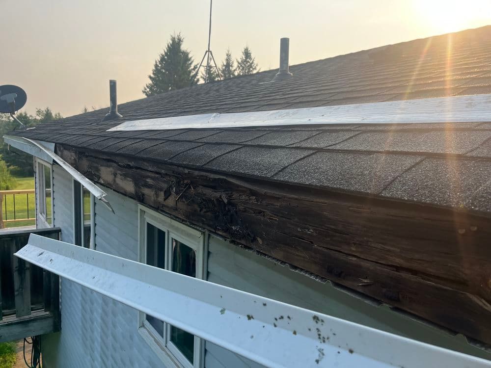 Damaged roof edge with exposed wood, showing signs of water damage and decay.
